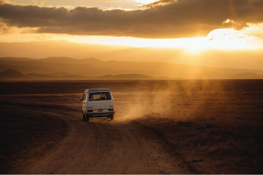 Van drives down dusty road at sunset